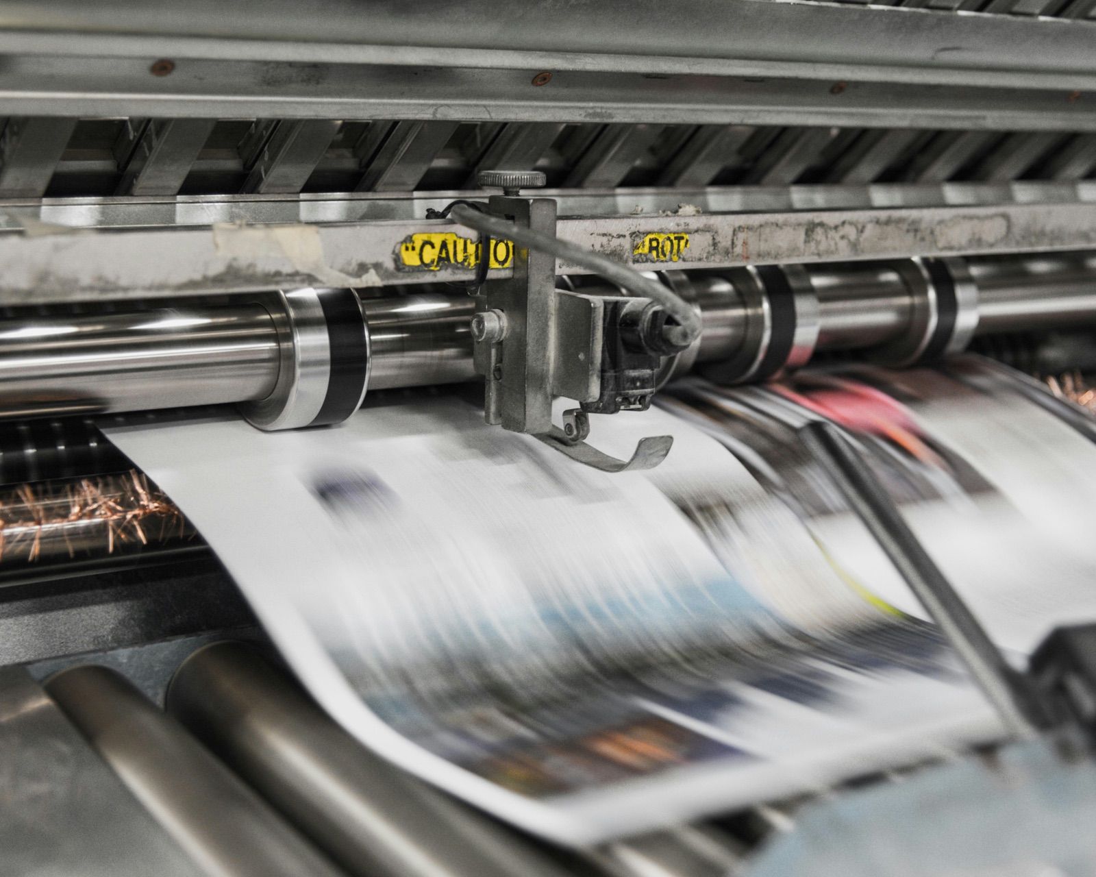 Printed sheets moving through the rollers of an offset press mid-run.
